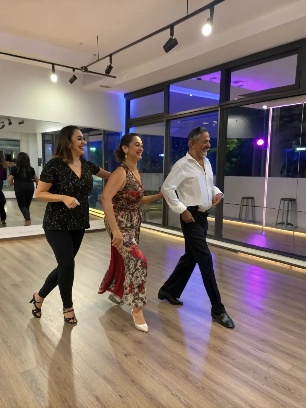 Adults of various ages learning a contemporary dance routine in a spacious studio. The dancers are focused and enjoying the movement.